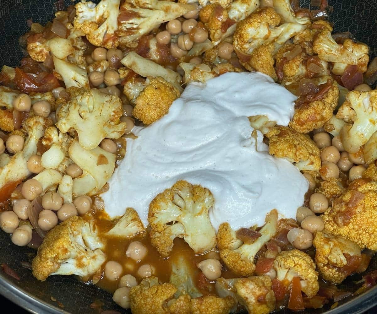 A pan has cauliflower tikka curry over the heat.
