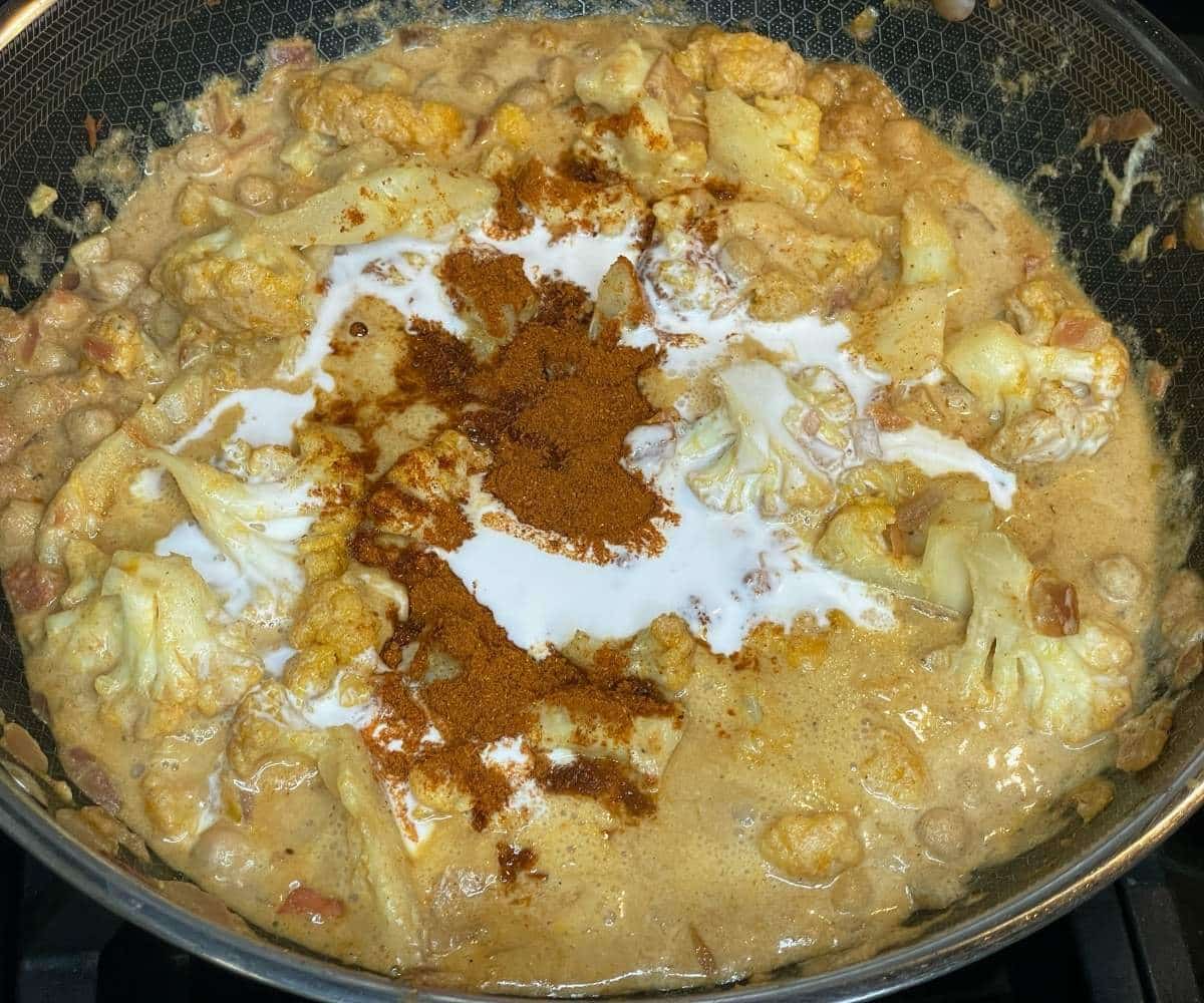 A pan is with vegan cauliflower tikka masala curry over the heat, with coconut milk and tikka spice. 