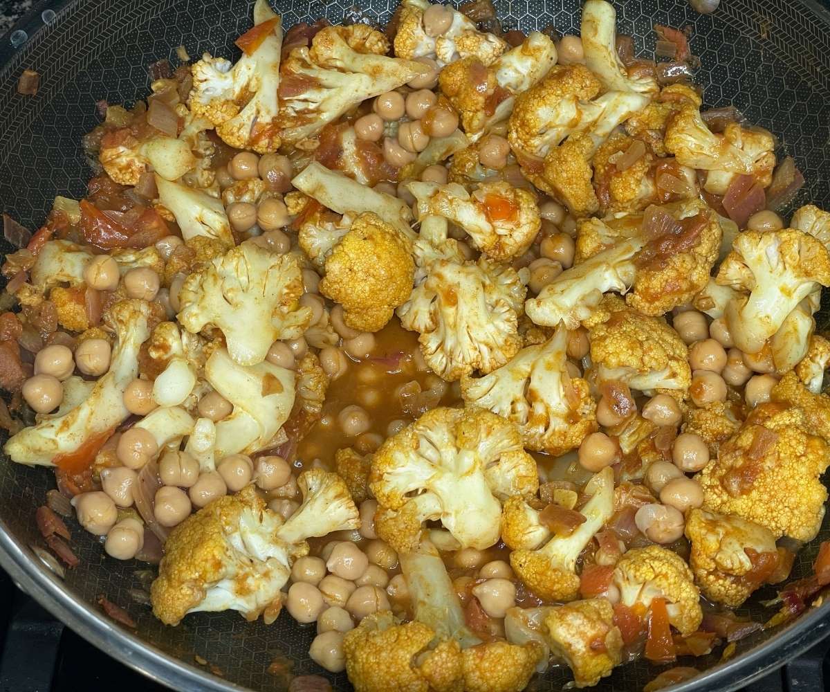 A pan is with spices, cauliflower, chickpeas for the curry.