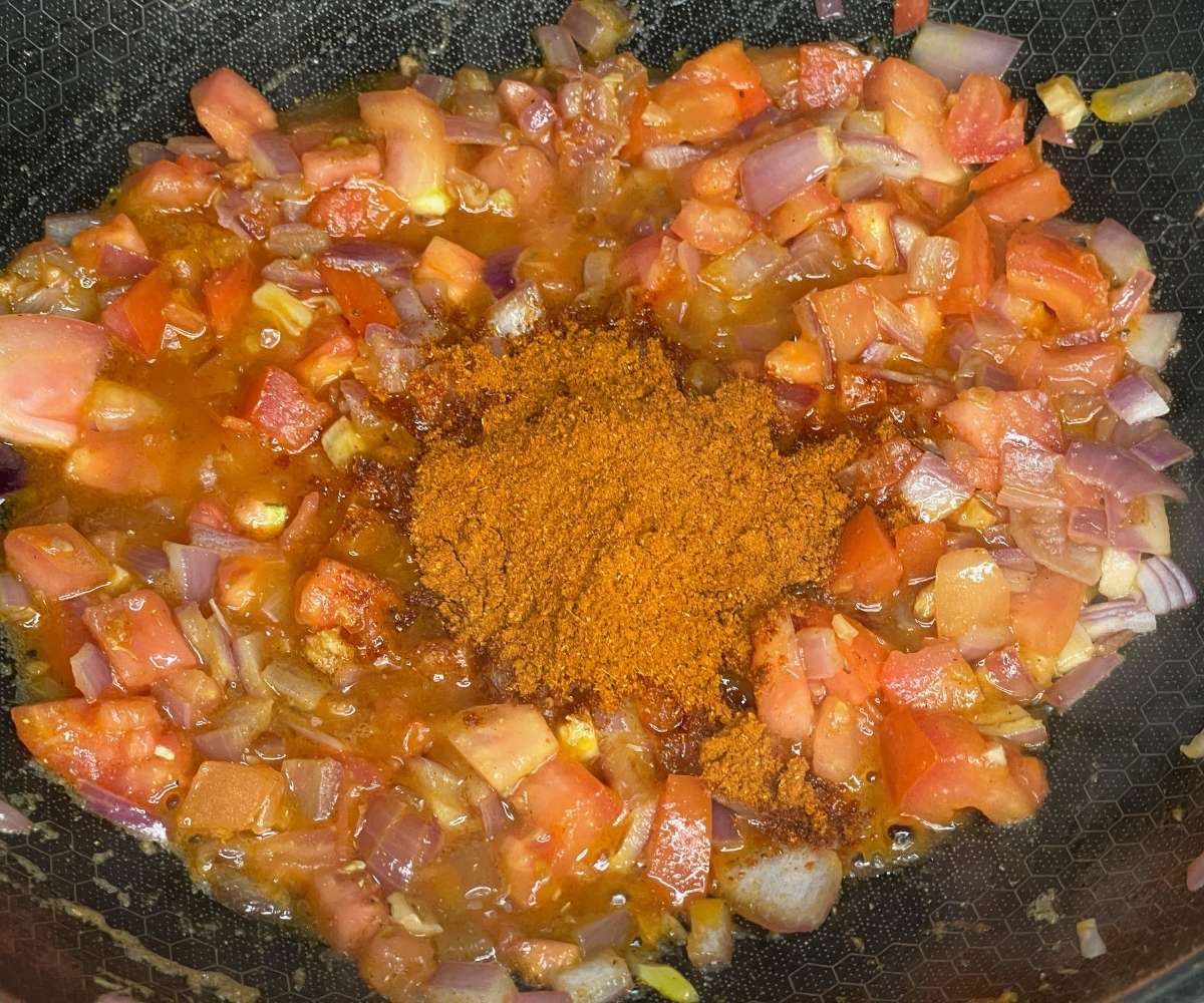 A pan is with tikka masala spice, tomatoes over the heat.