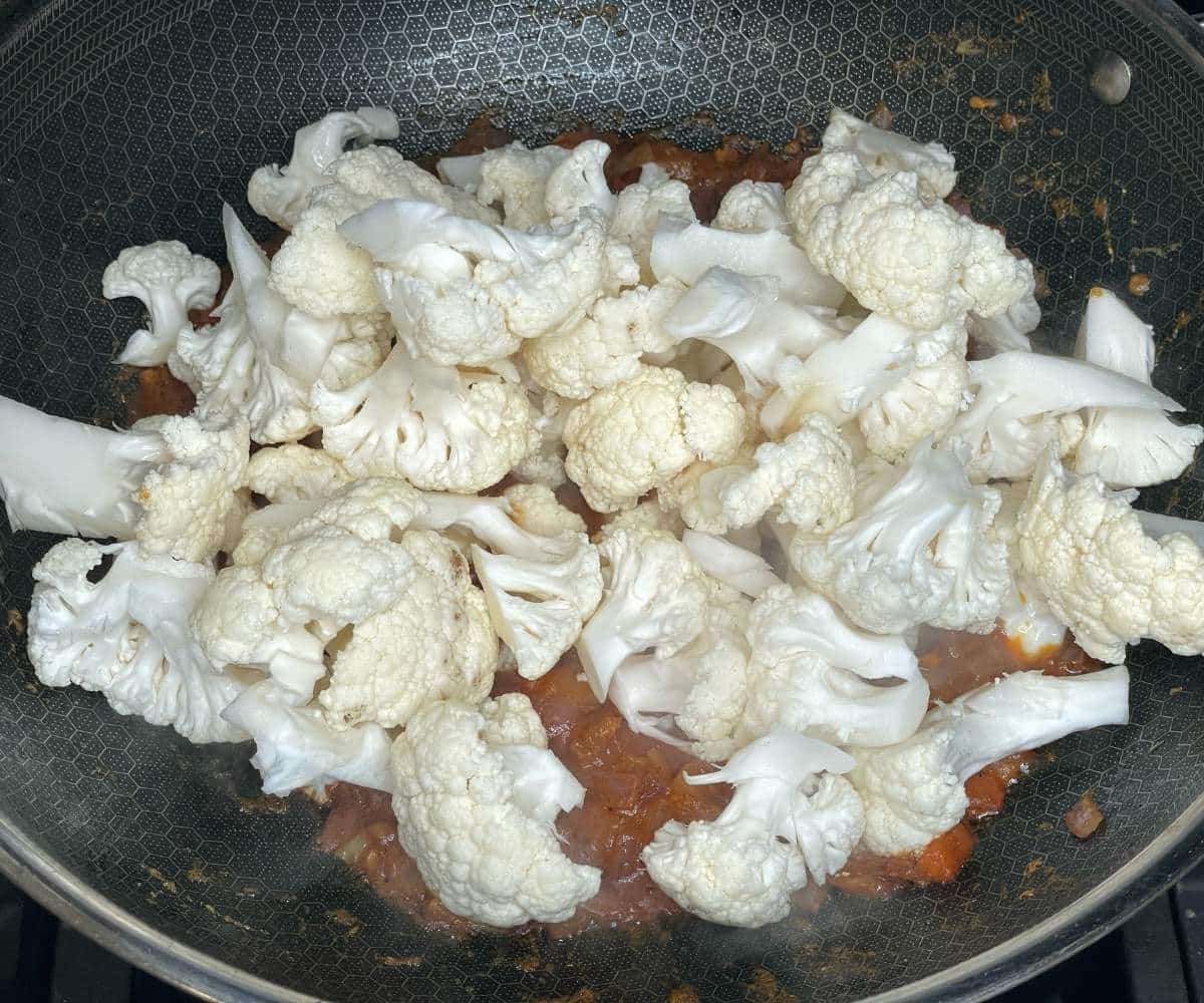 A pan has tikka masalas and cauliflower over the heat.