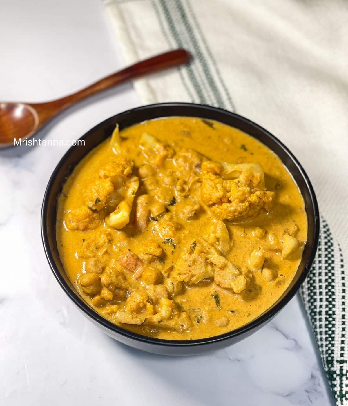 A bowl of vegan cauliflower tikka masala with chickpeas curry is on the marble table.